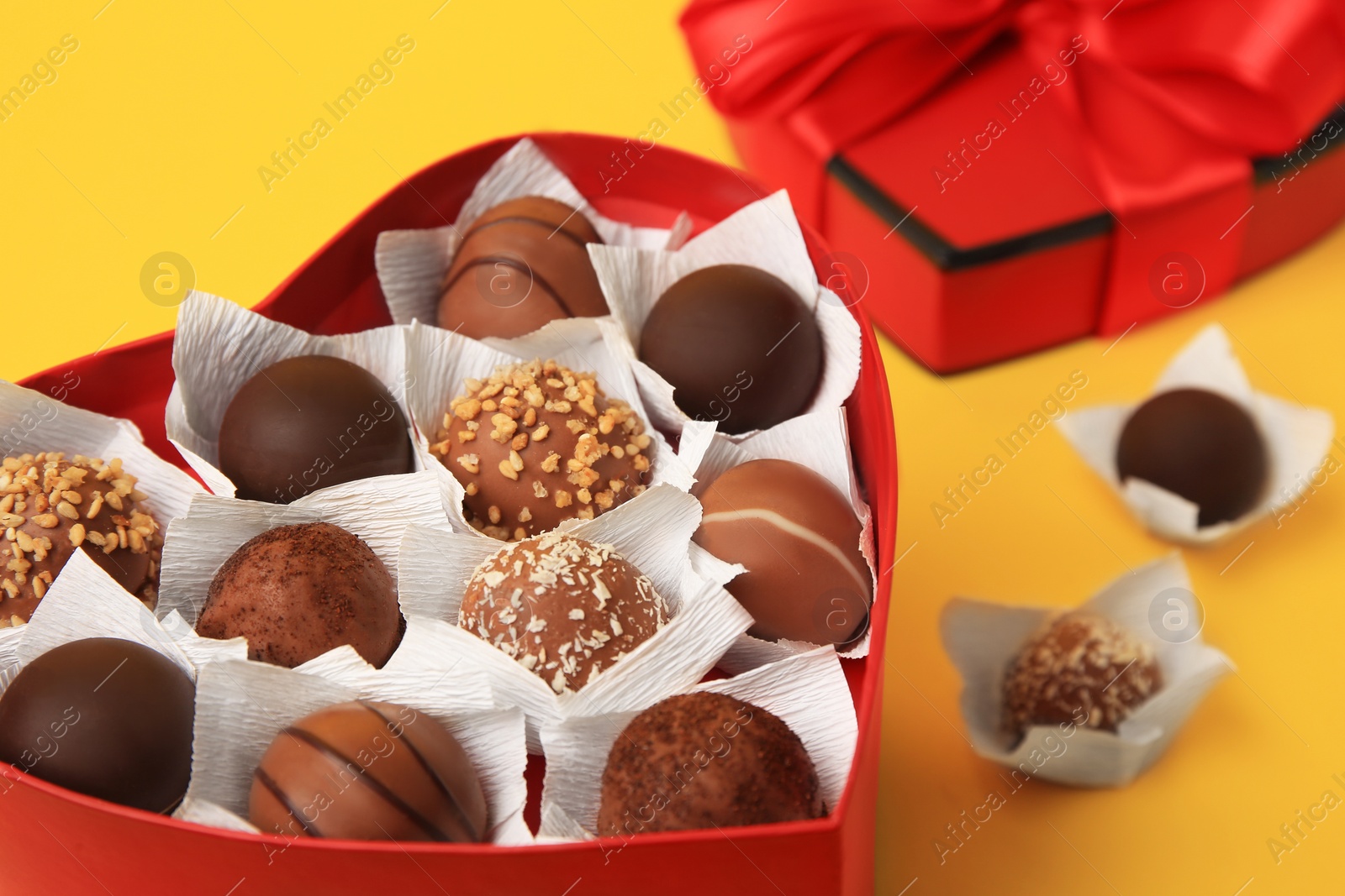 Photo of Heart shaped box with delicious chocolate candies on yellow background, closeup