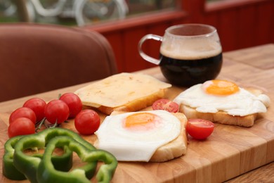 Tasty toasts with fried eggs, cheese and vegetables on wooden table indoors