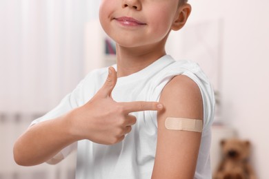 Photo of Boy pointing at sticking plaster after vaccination on his arm indoors, closeup