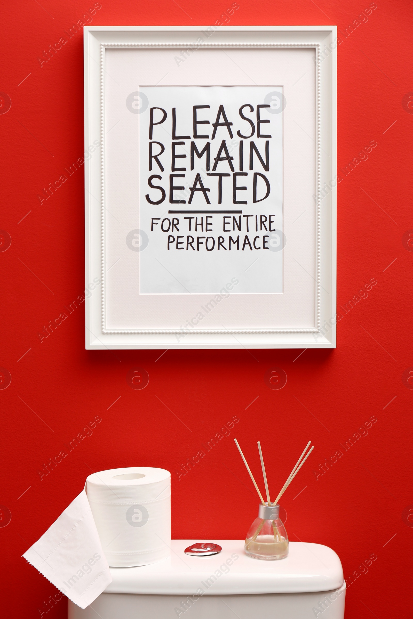 Photo of Toilet bowl and funny sign near red wall. Bathroom interior