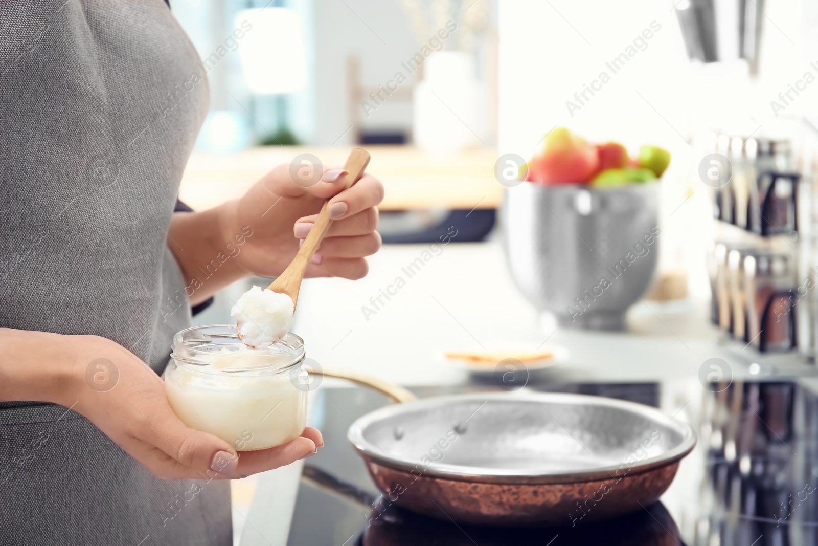 Photo of Woman putting coconut oil on frying pan in kitchen, closeup