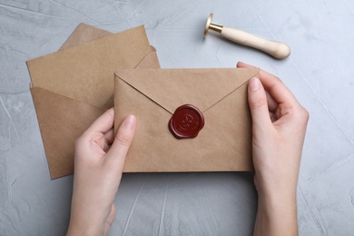 Photo of Woman holding envelope with wax seal at grey table, top view