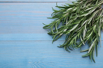Photo of Sprigs of rosemary on light blue wooden table, top view. Space for text