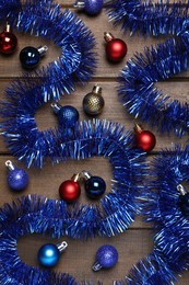 Photo of Bright tinsel and Christmas balls on wooden background, flat lay