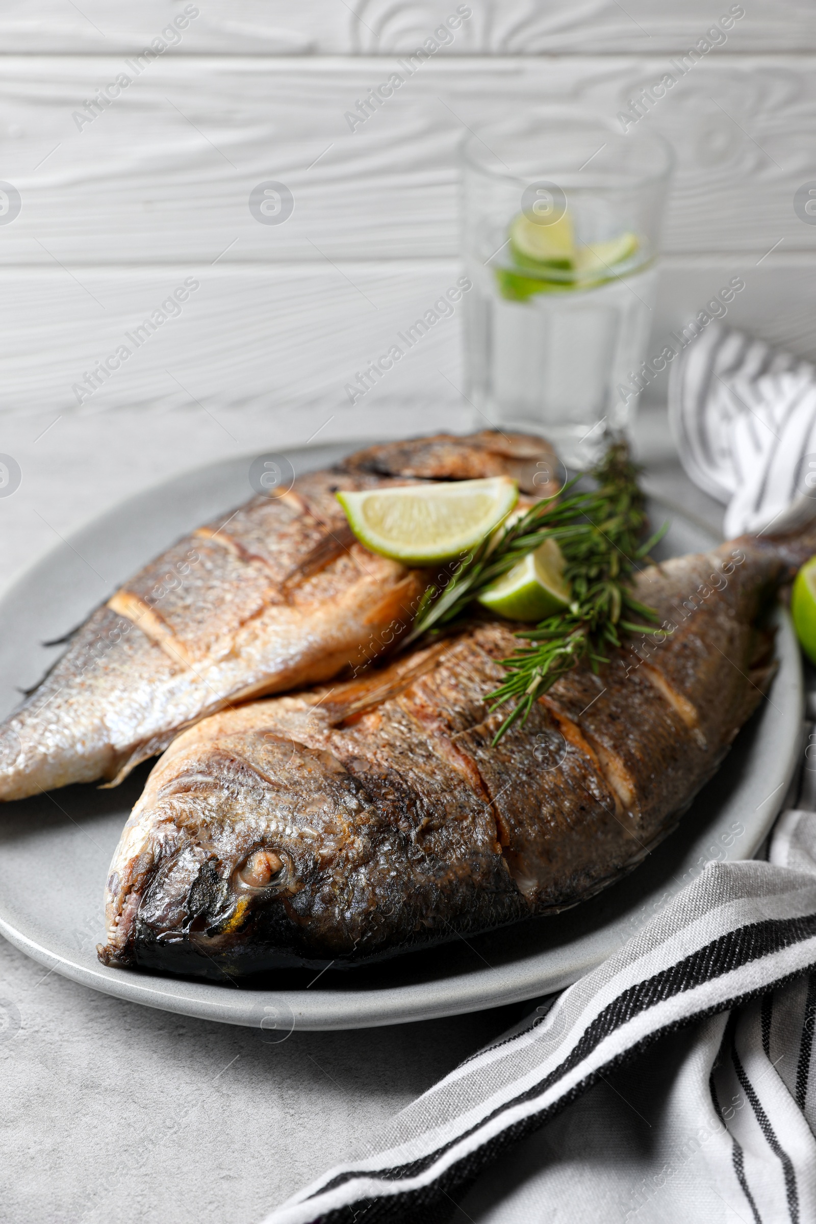 Photo of Delicious baked fish with rosemary and lime on grey table. Seafood