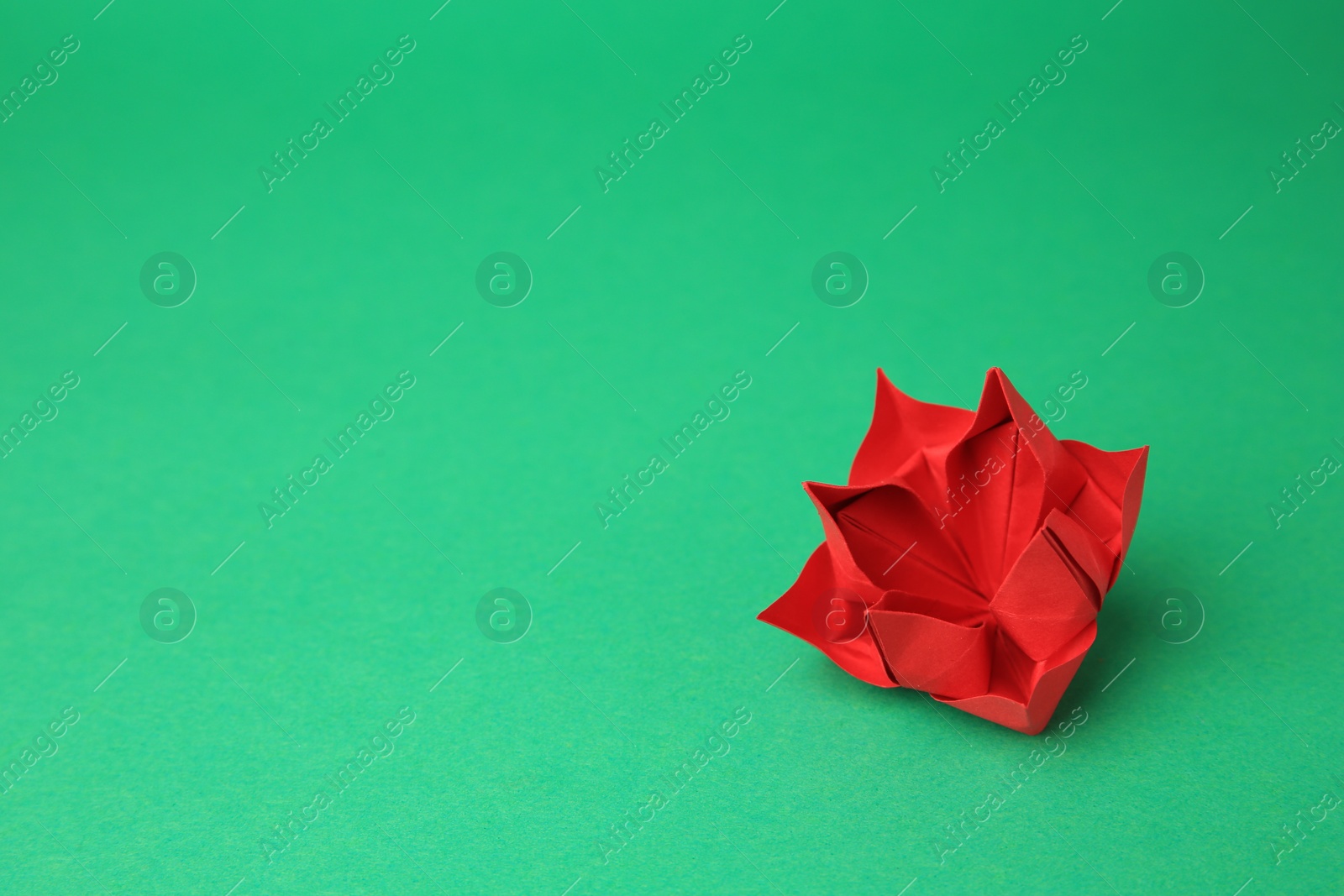 Photo of Origami art. Handmade red paper flower on green background, space for text