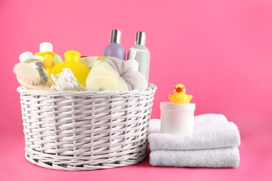Photo of Wicker basket with different baby cosmetic products, bathing accessories and toy on pink background