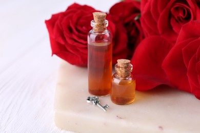 Photo of Bottles of love potion, red rose flowers and small key on white table, closeup. Space for text