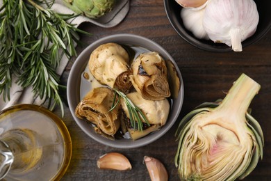 Photo of Bowl with delicious artichokes pickled in olive oil and ingredients on wooden table, flat lay