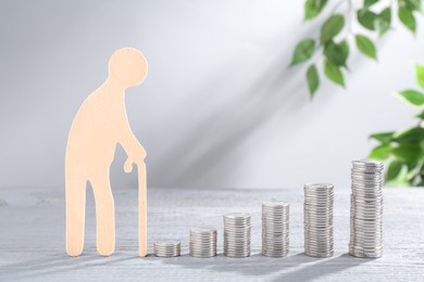 Pension savings. Figure of senior man and stacked coins on grey wooden table