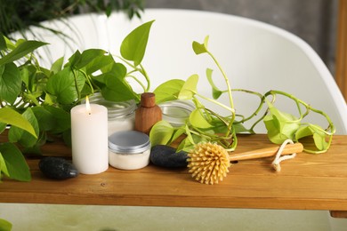 Photo of Composition with different spa products and green houseplants on tub tray in bathroom