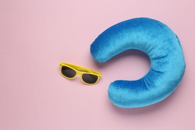 Photo of Light blue travel pillow and sunglasses on pink background, flat lay. Space for text