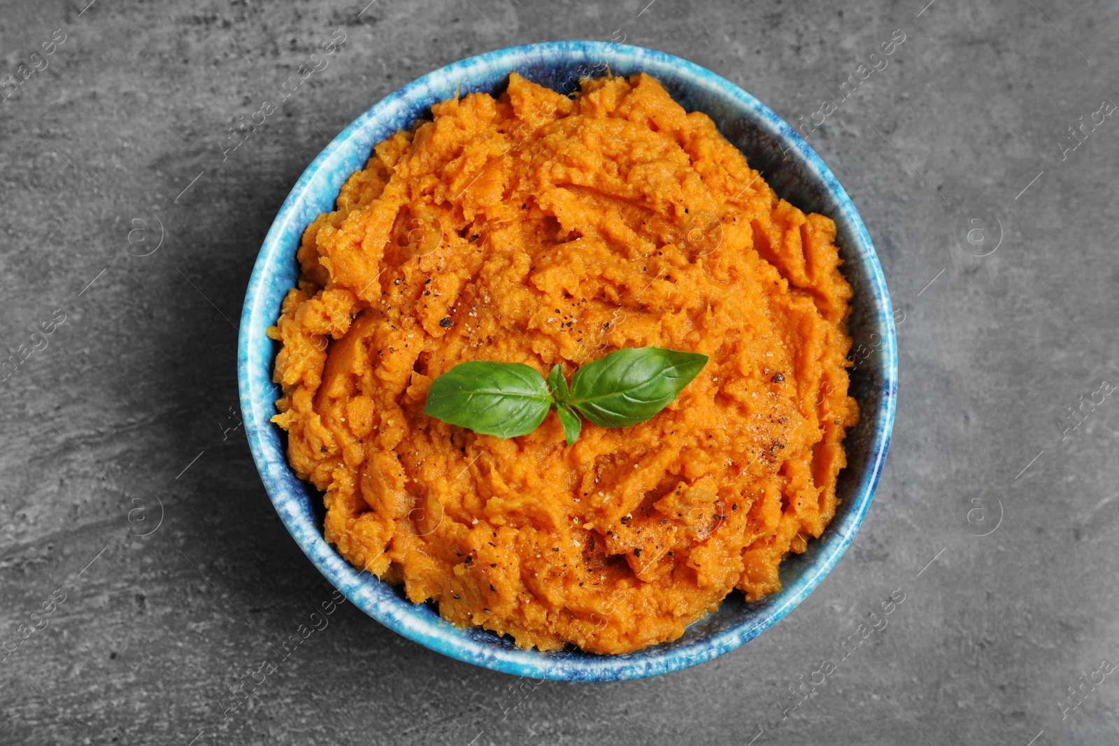 Photo of Bowl of tasty sweet potato puree on grey table, top view