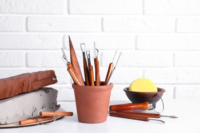 Clay and set of crafting tools on white textured table against brick wall