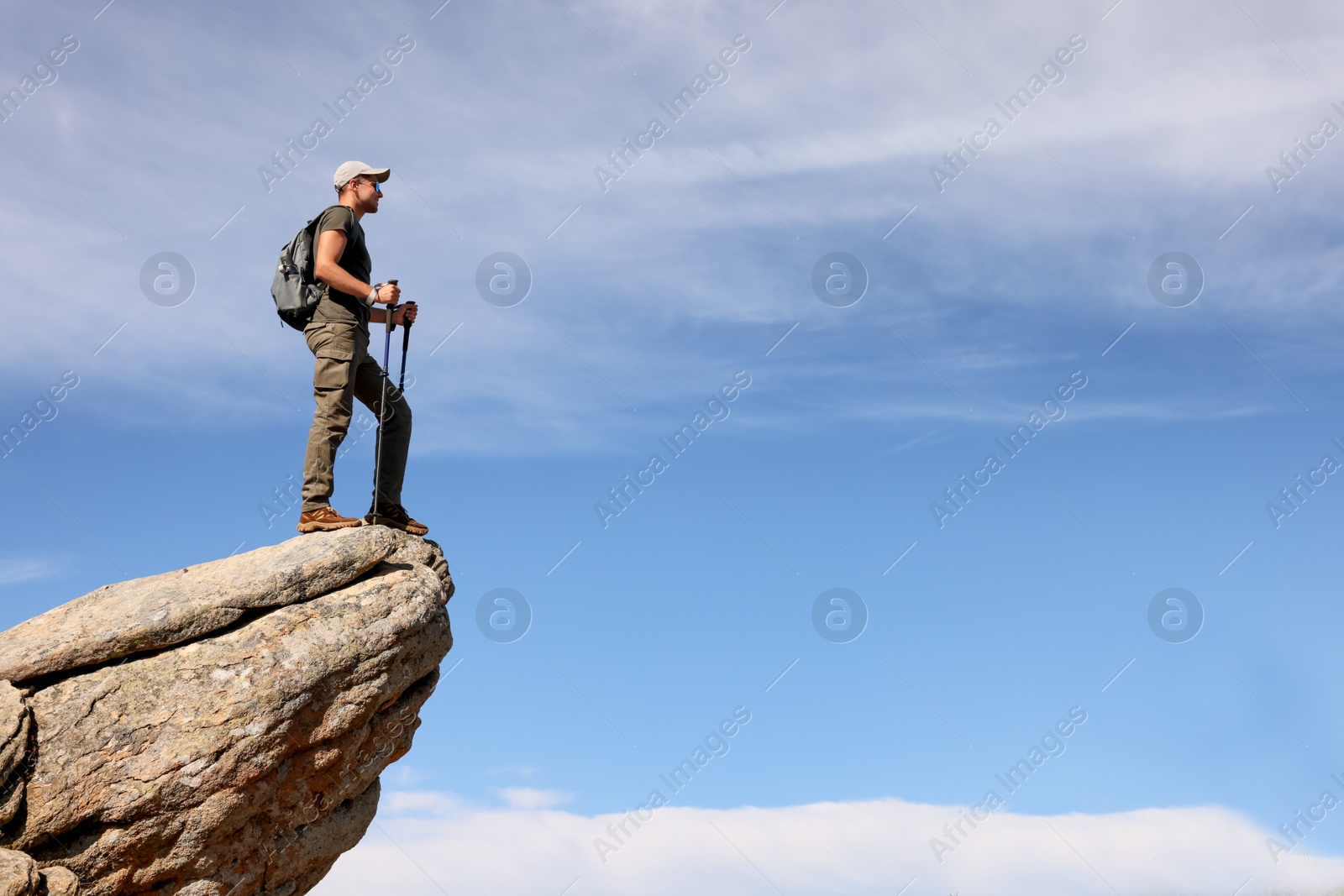 Photo of Man with backpack and trekking poles on rocky peak in mountains