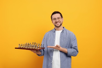 Smiling man showing chessboard with game pieces on orange background