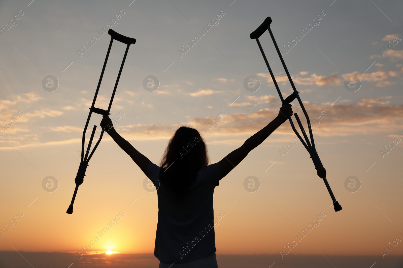 Photo of Woman holding axillary crutches outdoors at sunrise, back view. Healing miracle