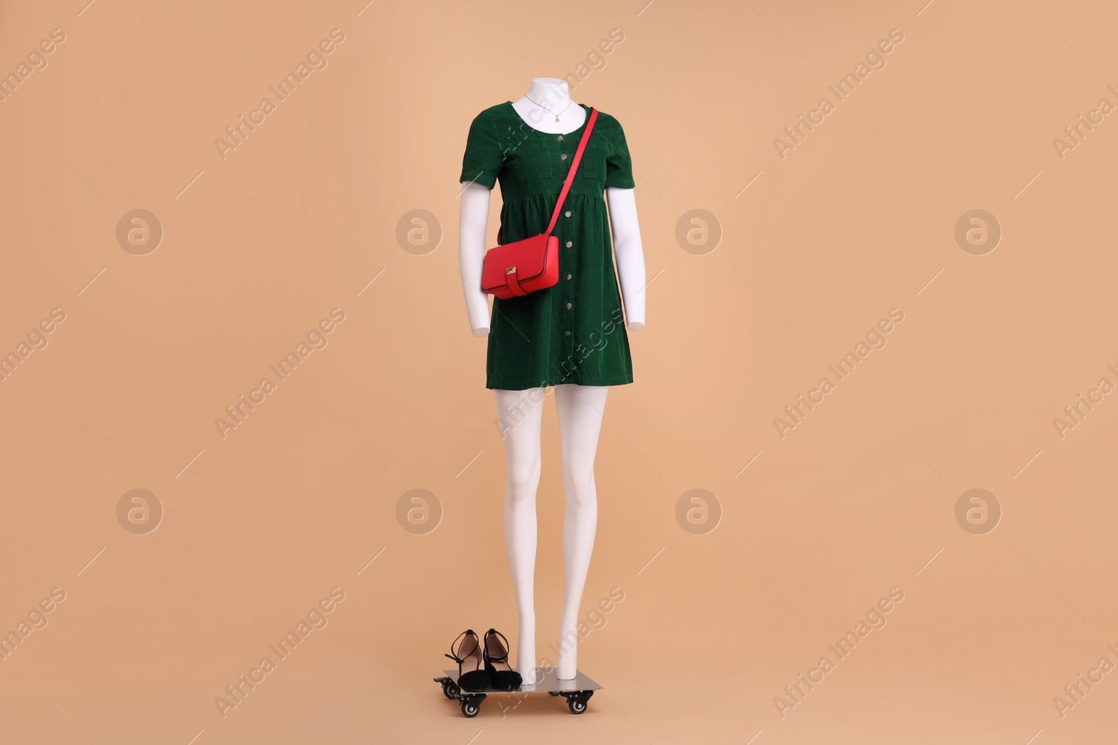Photo of Female mannequin with accessories and shoes dressed in dark green dress on beige background. Stylish outfit