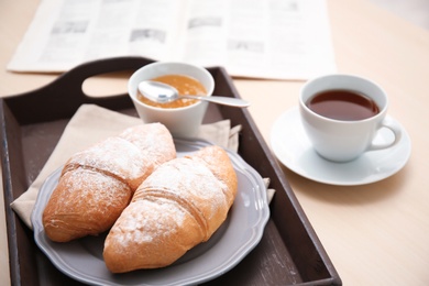 Photo of Tasty breakfast with fresh croissants, jam and cup of tea on tray