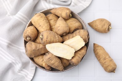 Whole and cut tubers of turnip rooted chervil in bowl on white tiled table, top view