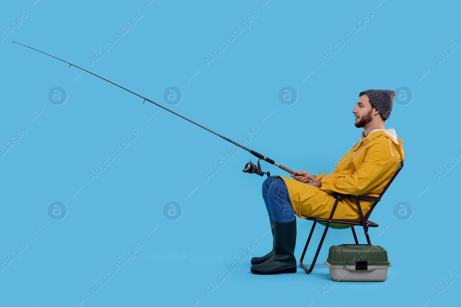 Photo of Fisherman with rod and tackle box on chair against light blue background