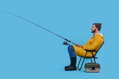 Fisherman with rod and tackle box on chair against light blue background