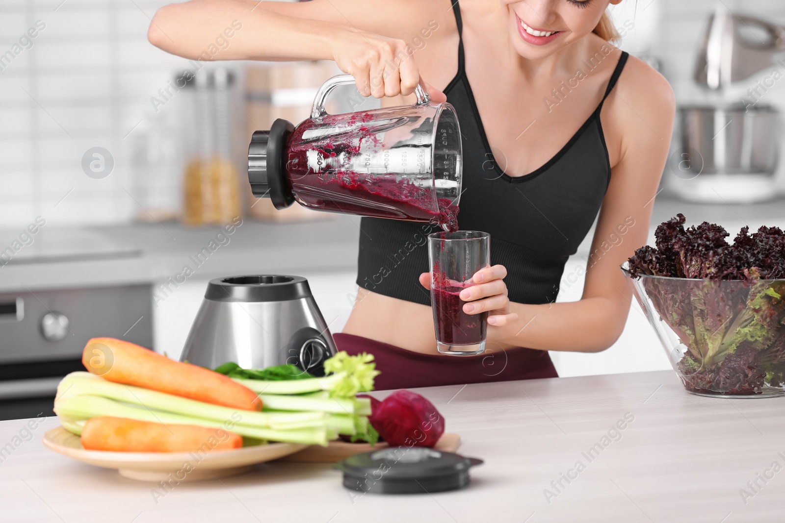 Photo of Young woman pouring tasty healthy smoothie into glass at table in kitchen