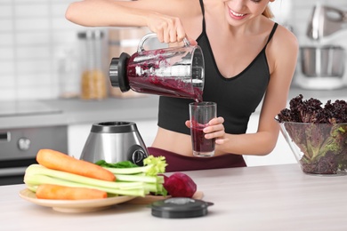 Photo of Young woman pouring tasty healthy smoothie into glass at table in kitchen