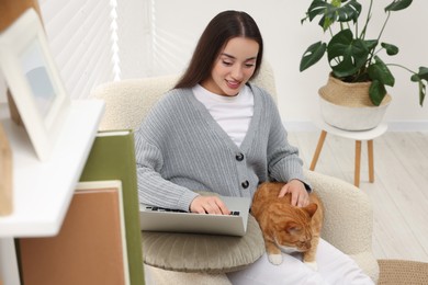 Photo of Happy woman working with laptop and petting cute cat at home