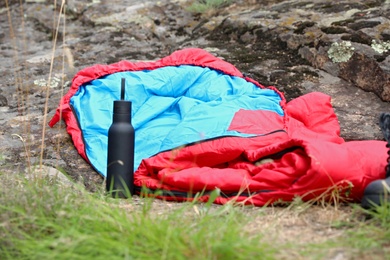 Photo of Sleeping bag and bottle outdoors. Camping gear