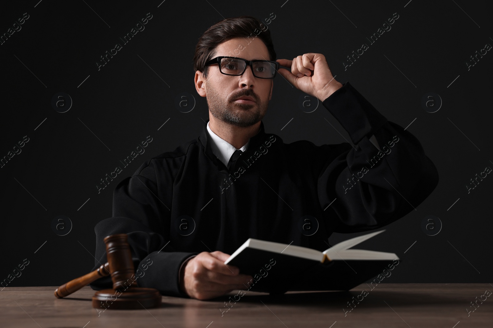 Photo of Judge with gavel and book sitting at wooden table against black background