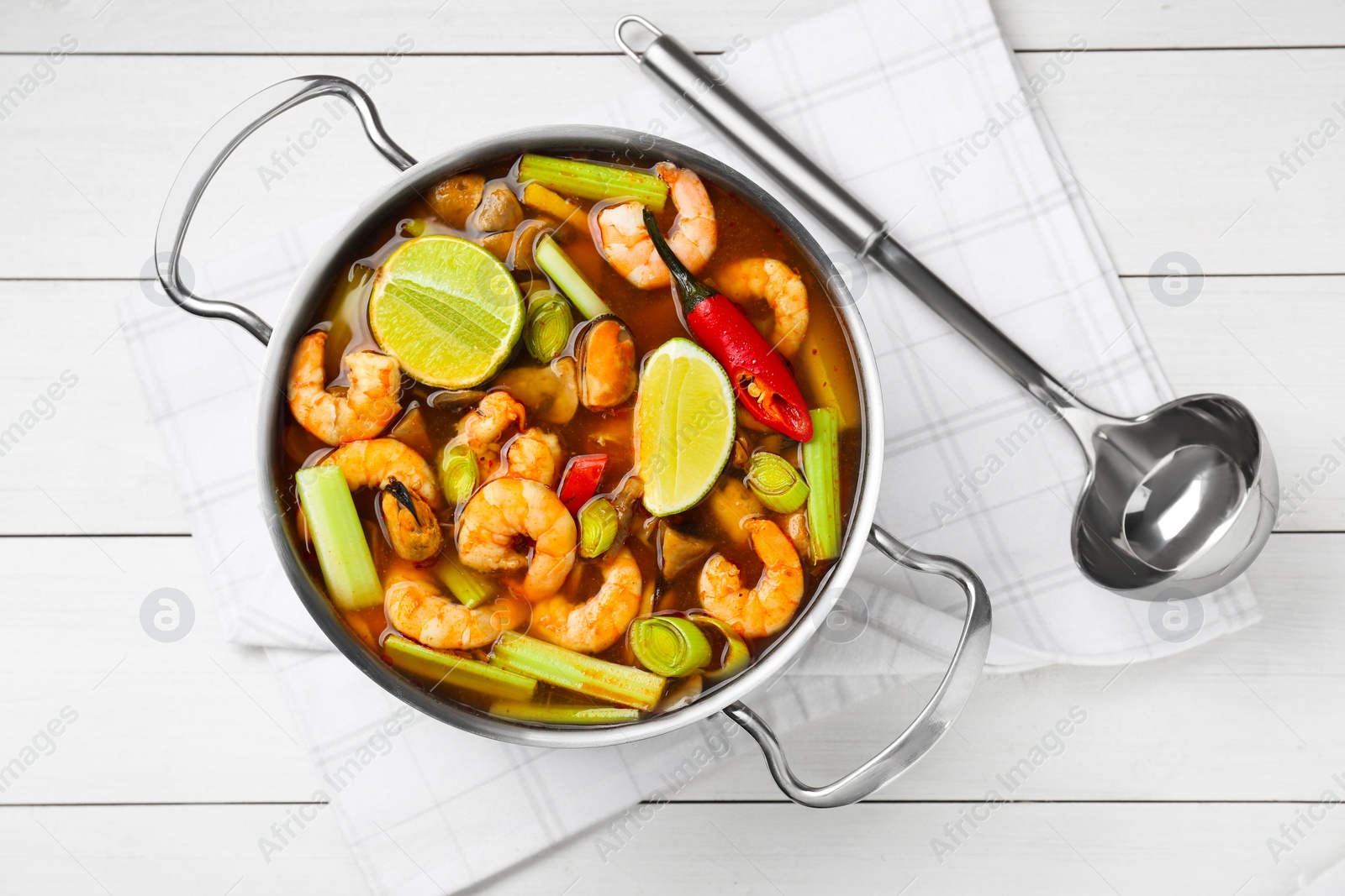 Photo of Saucepan with delicious Tom Yum soup on white wooden table, top view