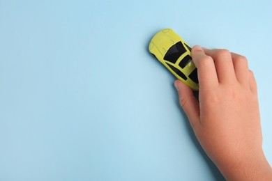 Photo of Child playing with toy car on light blue background, top view. Space for text