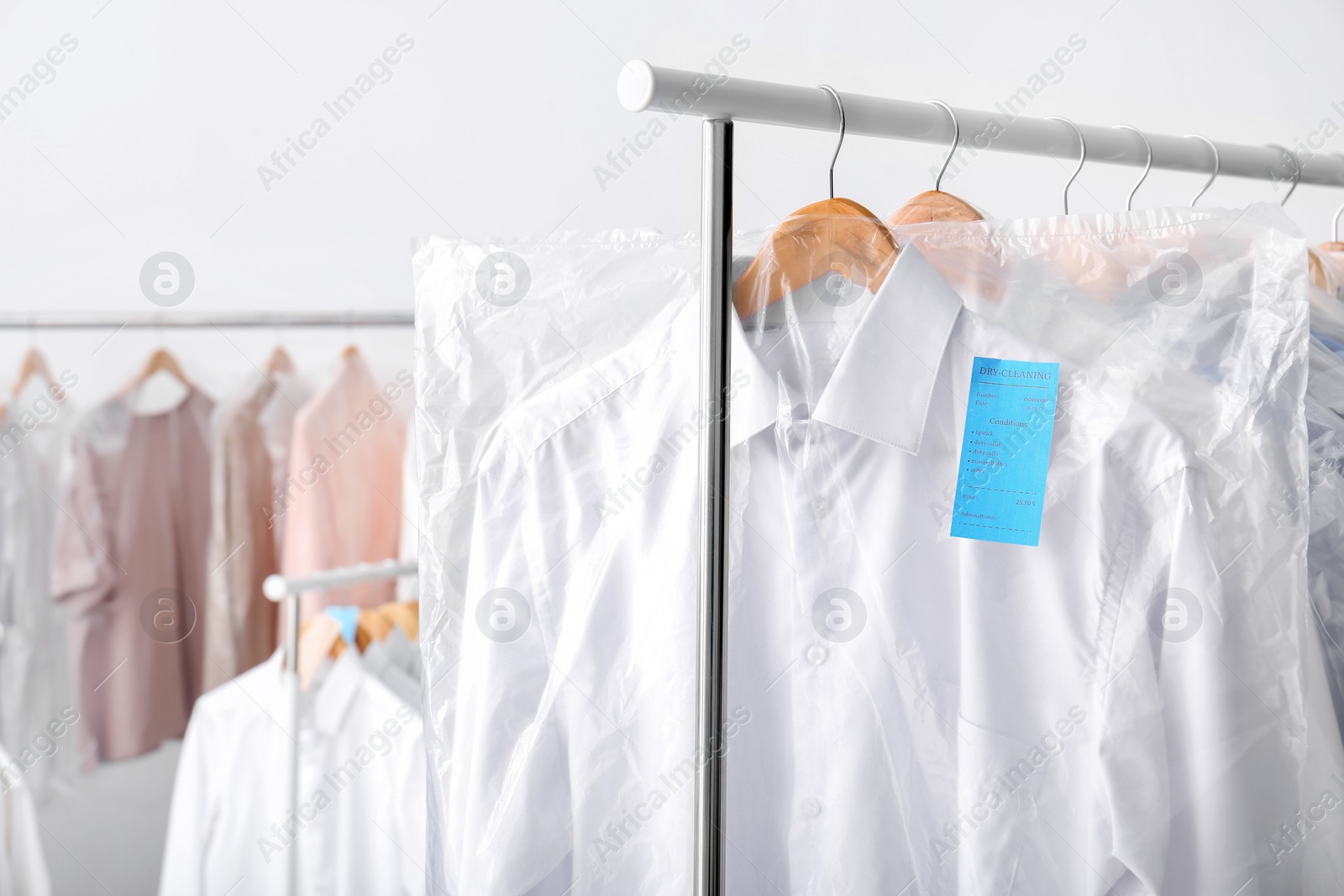 Photo of Rack with clean clothes on hangers after dry-cleaning indoors