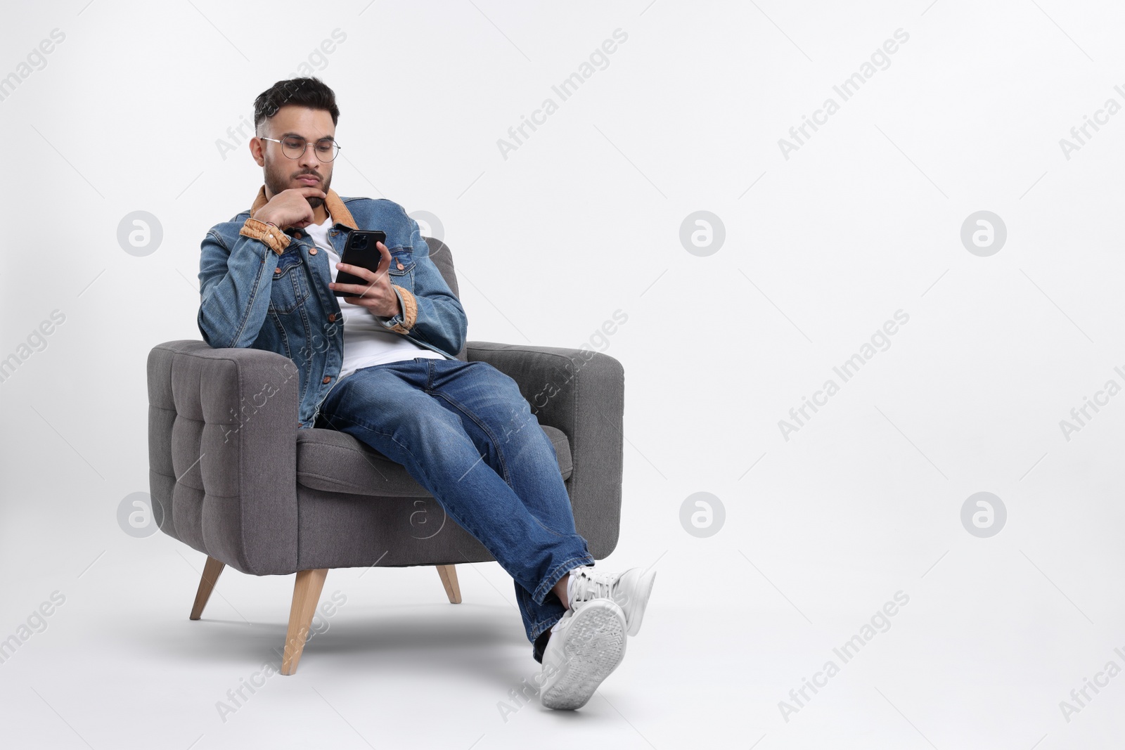 Photo of Handsome man using smartphone in armchair on white background, space for text