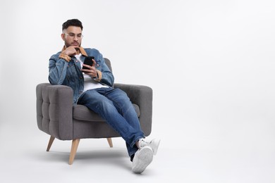 Photo of Handsome man using smartphone in armchair on white background, space for text