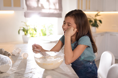 Photo of Cute little girl cooking dough in kitchen at home