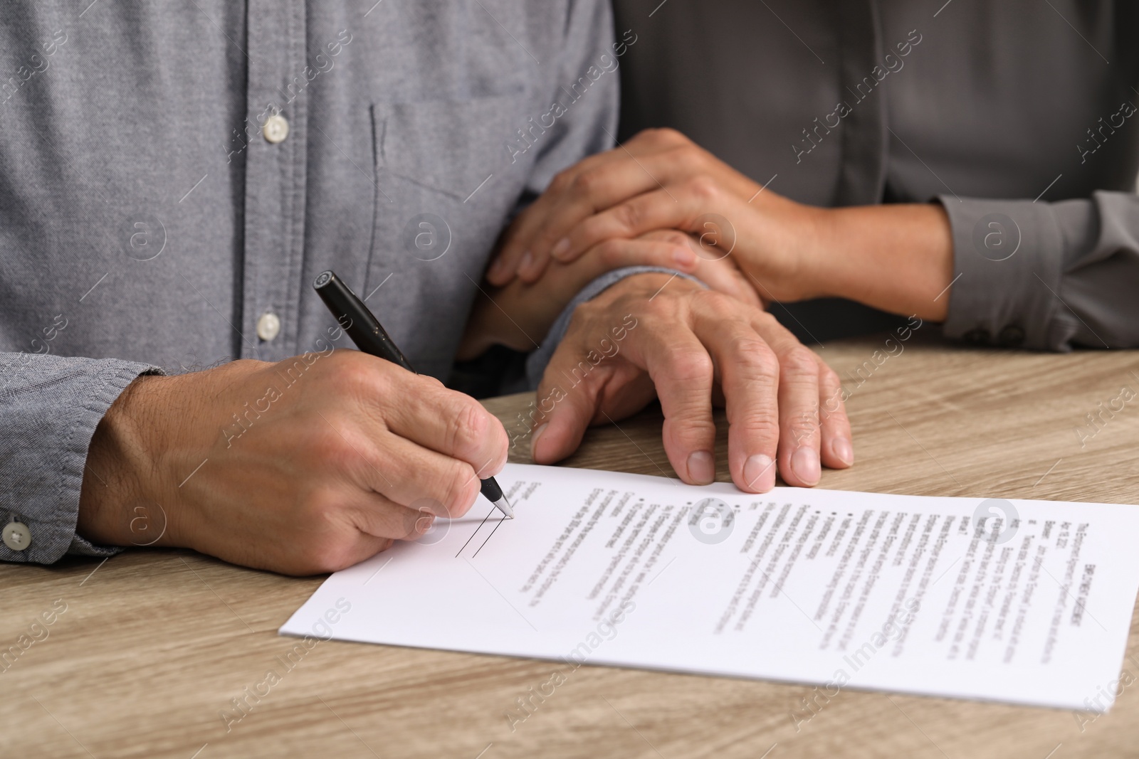 Photo of Couple signing document at wooden table, closeup