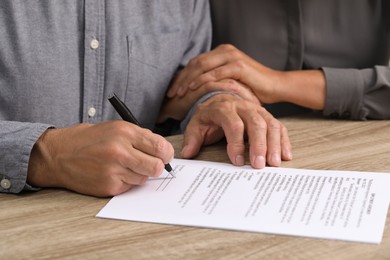 Photo of Couple signing document at wooden table, closeup