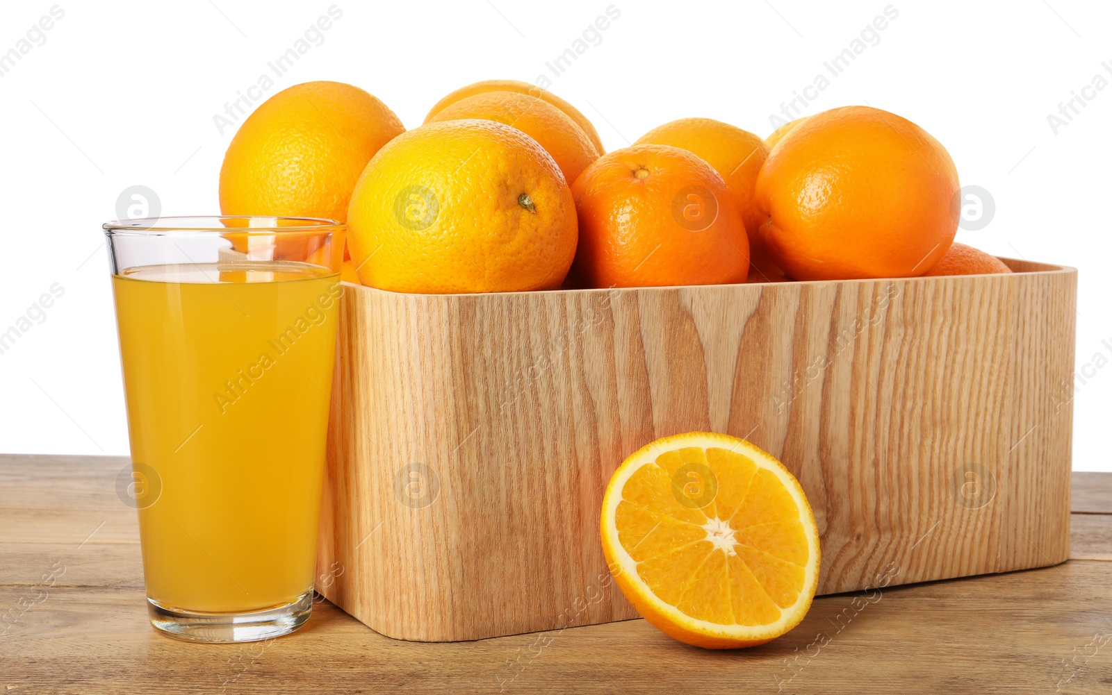 Photo of Fresh oranges in crate and glass of juice on wooden table against white background