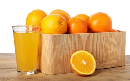 Fresh oranges in crate and glass of juice on wooden table against white background