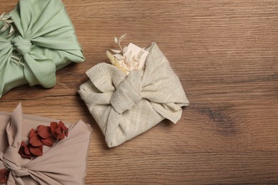 Photo of Furoshiki technique. Gifts packed in fabric and dry leaves on wooden table, flat lay. Space for text