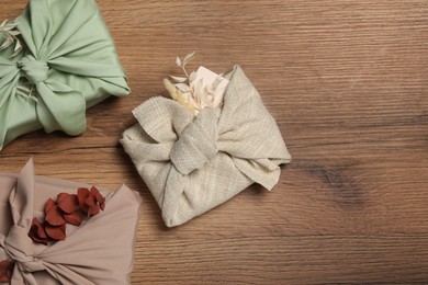 Furoshiki technique. Gifts packed in fabric and dry leaves on wooden table, flat lay. Space for text