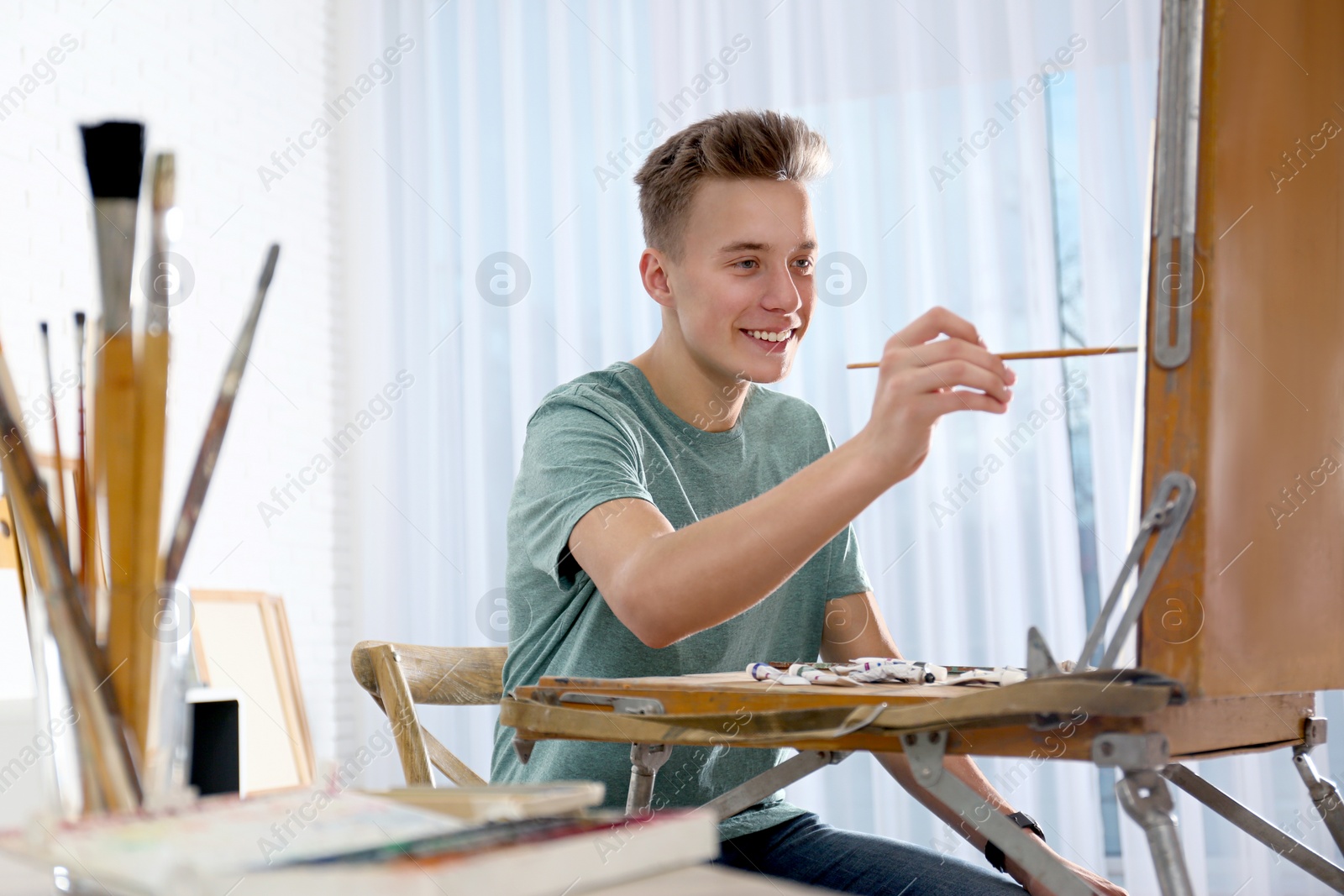 Photo of Teenage boy painting on easel in workshop, space for text. Hobby club