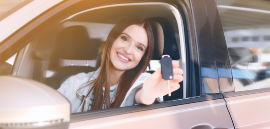 Image of Happy woman with car key sitting in modern auto outdoors on sunny day. Banner design