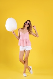 Photo of Happy young woman with cotton candy on yellow background