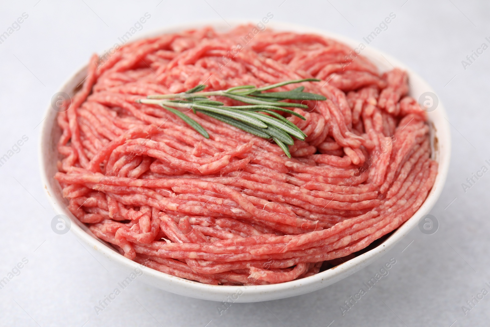 Photo of Fresh raw ground meat and rosemary in bowl on light table, closeup