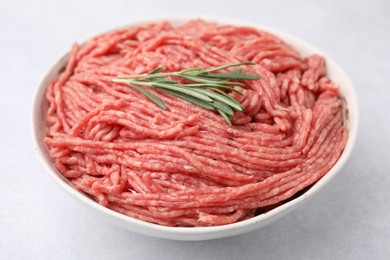 Fresh raw ground meat and rosemary in bowl on light table, closeup