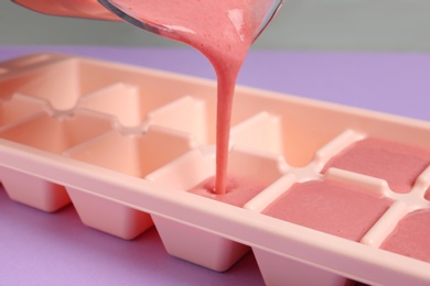 Photo of Pouring smoothie into ice cube tray on table, closeup