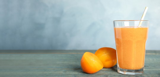 Image of Tasty persimmon smoothie with straw and fresh fruit on wooden table against light blue background, space for text. Banner design